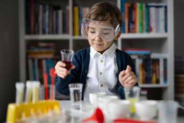 One small caucasian boy scientist five years old wearing protective eyeglasses sitting at the table playing with chemistry equipment toy preforming experiment learning and education concept front view