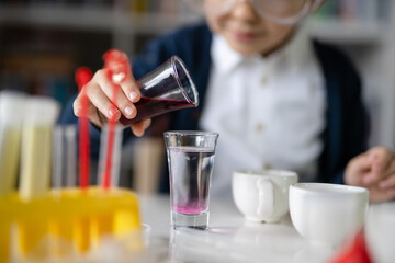 Close up on hand of One small caucasian boy scientist five years old sitting at the table playing with chemistry equipment toy preforming experiment learning and education concept front view