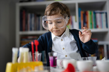 One small caucasian boy scientist five years old wearing protective eyeglasses sitting at the table playing with chemistry equipment toy preforming experiment learning and education concept front view