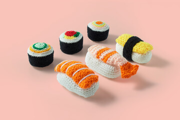 Assorted set of maki sushi rolls and nigiri sushi handmade in crochet and colored wool. Sushi set isolated on a pink background. Sushi crochet amigurumi - obrazy, fototapety, plakaty