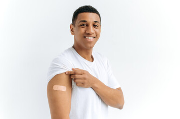 Mixed race happy guy stands on isolated white background with a plaster on his shoulder, received a...