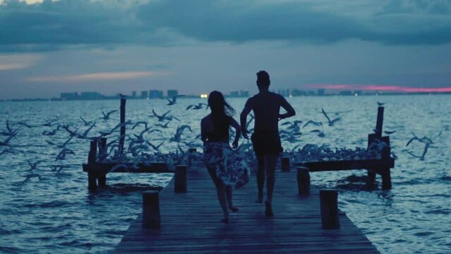 Pareja corriendo sobre el muelle alegres junto con las gaviotas, de espalda