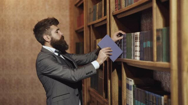 Portrait Of Authentic Man With Beard Reading Book In The Hand On Bookshelf Background. Businessman In Classic Suit Read Book. Old Fashion Business People. Man Picking A Book In A Library.