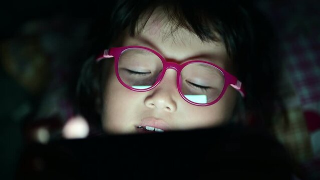 Child girl watching movie or play game in tablet device at night time in bed room eye closeup