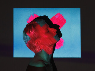 fashion androgyne woman with projection of neon pink cross shape on her face