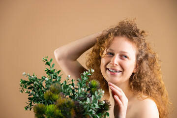 Portrait of a beautiful young woman with red hair and natural makeup with a bouquet of green flowers in front of her.