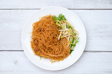 fried noodles vermicelli on white plate , Chinese styled fried noodle with bean sprout and coriander on wooden table - Thai food