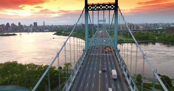 Numerous cars moving quickly along Triborough Bridge in New York. Football pitch and car park on both sides from the bridge. Cityscape under beautiful pink sky at backdrop.