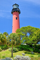 Historic red brick Jupiter lighthouse with lush green vegetation against blue skies at Jupiter Inlet, Florida © Ryan Tishken