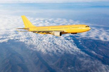 Yellow passenger plane in flight. The plane is flying over the clouds. Side view of aircraft.