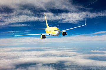 Fototapeta premium Yellow passenger jet plane in the sky. Airplane flies high through the clouds. Aircraft front view.