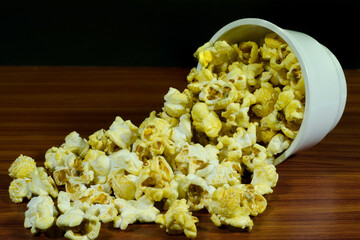 yellow and white popcorn in a white cup and some overflowed onto the wooden floor.