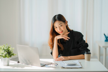 Asian businesswoman analyzing a report pointing to a graph with a pen, laptop, and calculator. In workstation, accountant, online marketing concept, e-commerce, landscape image.