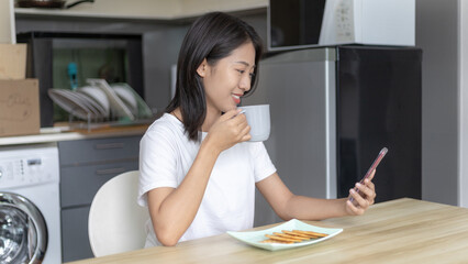 Asian woman eats breakfast with crackers (Healthy whole grain) and juice, Use your phone or mobile phone to search for morning news, Small room in condominium background, Wake-up activities.
