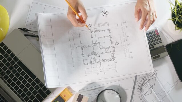 Architectural workplace. Architect open drawing paper to review and design of house editing with pencil on plan blueprint paper on table desk at architecture office, engineer sketching blueprint