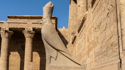 An ancient granite statue of a falcon in a crown in the temple of Horus in Edfu. The background is...