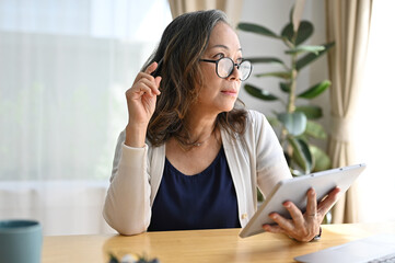 Successful asian retired woman using digital tablet touchpad in the living room