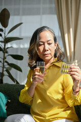 Portrait of a sick asian aged woman drinking water and taking a medicine