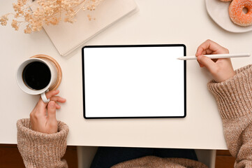 A female freelance blogger in comfy sweater sipping morning coffee and using tablet