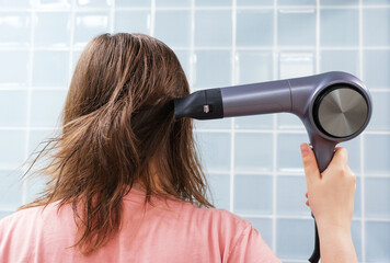 Young woman drying her hair with hairdryer in the bathroom close-up back view.
