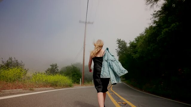 Woman wearing little black dress and holding trucker jacket on her shoulder. Slow motion video of nomadic journey across the the USA. High quality 4k footage