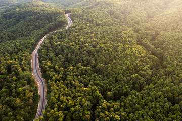 Top view of countryside road passing through the green forrest and mountain