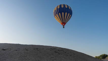 A bright yellow-blue balloon is flying in a clear azure sky over a sand dune. Close-up. Copy space....
