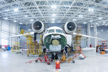 Front view of the white transport airplane in the hangar. Aircraft under maintenance. Checking...