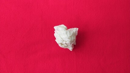 One single twisted used dirty leftover white tissue paper or napkin scattered and isolated on red...