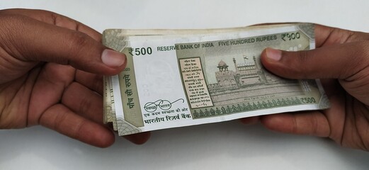 Hand giving or transferring stack of five hundred rupee new indian currency bank paper notes on...