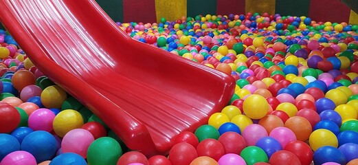 Children's playground with red color plastic slider and colorful plastic balls in pool for kids and...