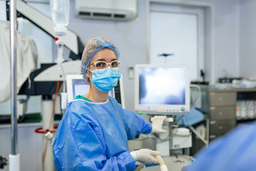 Anesthetist Working In Operating Theatre Wearing Protecive Gear checking monitors while sedating patient before surgical procedure in hospital