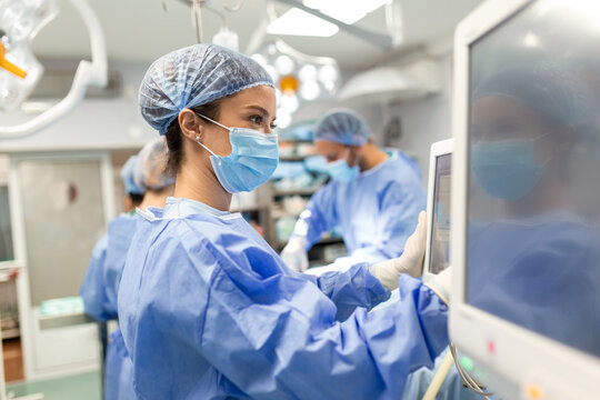 Diverse Team of Professional Surgeons Performing Invasive Surgery on a Patient in the Hospital Operating Room. Nurse Hands Out Instruments to surgeon, Anesthesiologist Monitors Vitals.