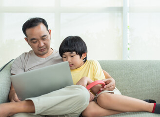 Little boy  relaxing on the sofa at home with his father watching funny videos on laptop together. A father is so happy with his preschool son in the living room. 