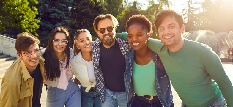 Young Diverse Friends Having Great Time Together. Group Portrait Of Happy Caucasian, Afro American And Asian People Standing In Warm Evening Sunlight, Hugging Each Other, Looking At Camera And Smiling
