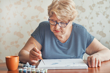 Attractive old woman painting by numbers at home. Inspirational hobby and art therapy. Selective focus