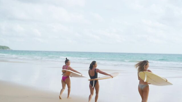 4K Group of Asian woman surfer in swimwear holding surfboard walking together on tropical beach in sunny day. Female friends enjoy outdoor activity lifestyle water sport surfing on summer vacation