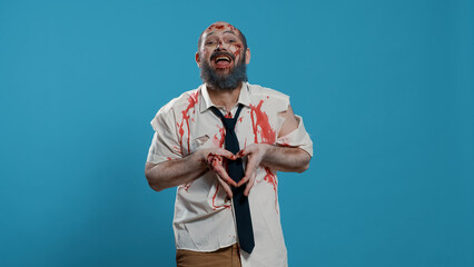 Creepy goofy zombie sending air kisses to camera while standing on blue background. Bizarre looking doomsday brain-eating monster with deep and bloody wounds and scars sending kisses. Studio shot