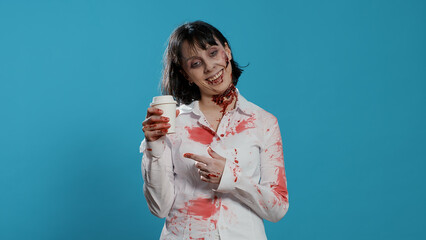 Creepy looking zombie with deep scars smelling coffee from a cup on blue background. Frightening...