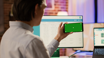 Entrepreneur looking at horizontal greenscreen on smartphone, using blank chroma key with mockup copyspace template and isolated background. Mobile phone application on display.