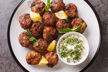 Juicy Baked Greek Meatballs Keftedakia with tzatziki sauce and lemon on a white plate on a table. Horizontal top view from above