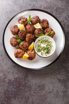 Keftedakia fried greek meatballs with tzatziki sauce and lemon on a white plate on a table. Vertical top view from above