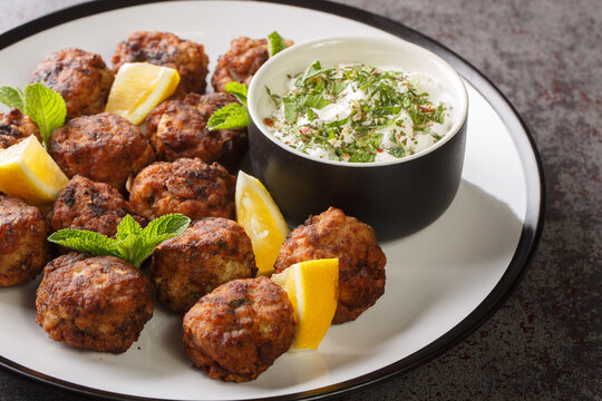 Juicy Baked Greek Meatballs Keftedakia with tzatziki sauce and lemon on a white plate on a table. Horizontal
