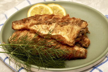 fried fish with lemon and herbs on a plate on the table
