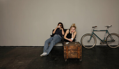 Two exhausted young women  with hangover after a party sit in chairs in studio indoors, having...