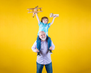 Grandfather and grandson piggyback ride with plane and wooden toy truck. Men generation granddad and grandchild.
