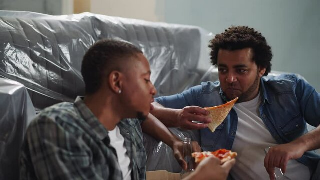 Cheerful African-American man eats pizza and talks to friend