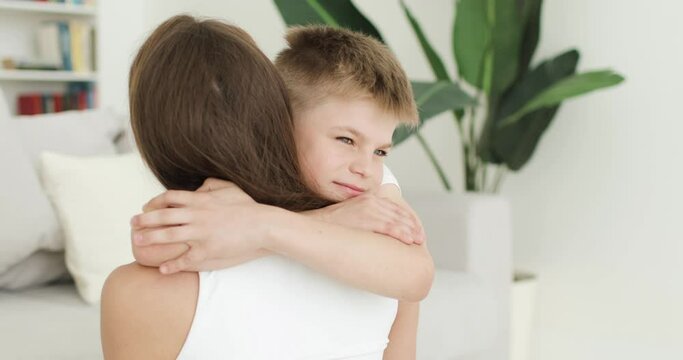 Young mom and little son have fun at home in the living room. Close-up of boy hugging and kissing his mom. Active family, parent and child spend time together enjoying fun activities.