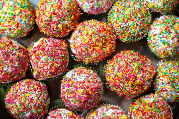Homemade cupcakes decorated sugar sprinkles top view. Group of homemade vanilla muffins white glazed multicolored decoration. Sweet cake background.