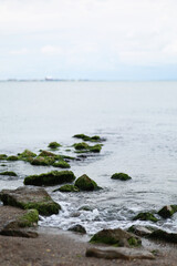 Stones covered with moss laying in open water. Water horizon. Small waves among stones 